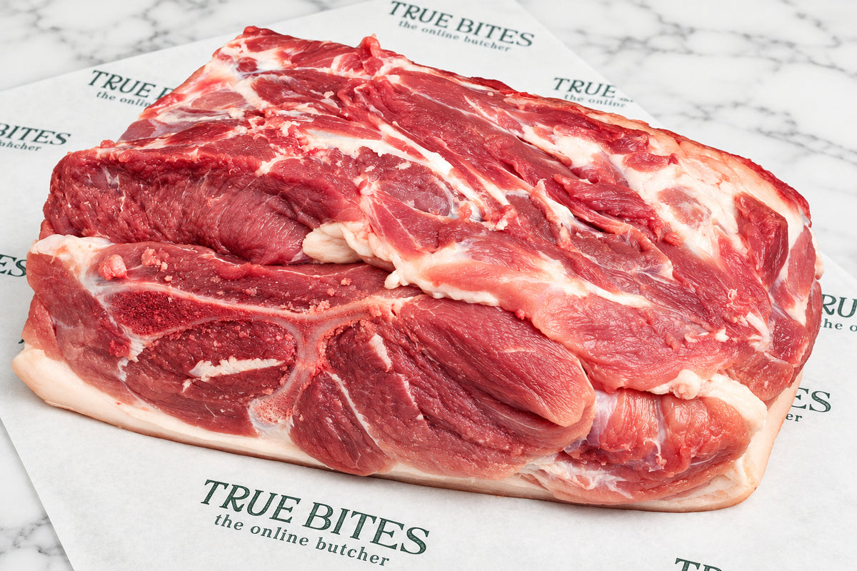 A raw whole pork butt with white fat marbling, placed on branded butcher paper with scattered coarse salt on a dark wooden surface. The paper shows the visible brand text 'TRUE BITES the online butcher'.