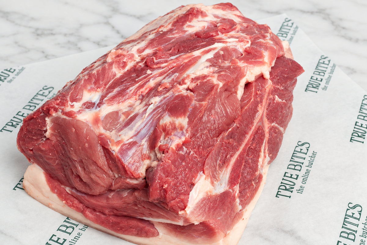 A large raw whole pork butt with white fat layers, resting on branded white butcher paper over a dark wooden surface.