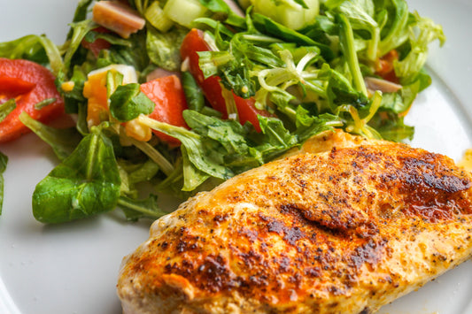 cooked chicken breast on a plate with fresh salad