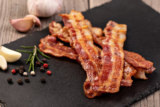 cooked dry cured streaky bacon on a black slate