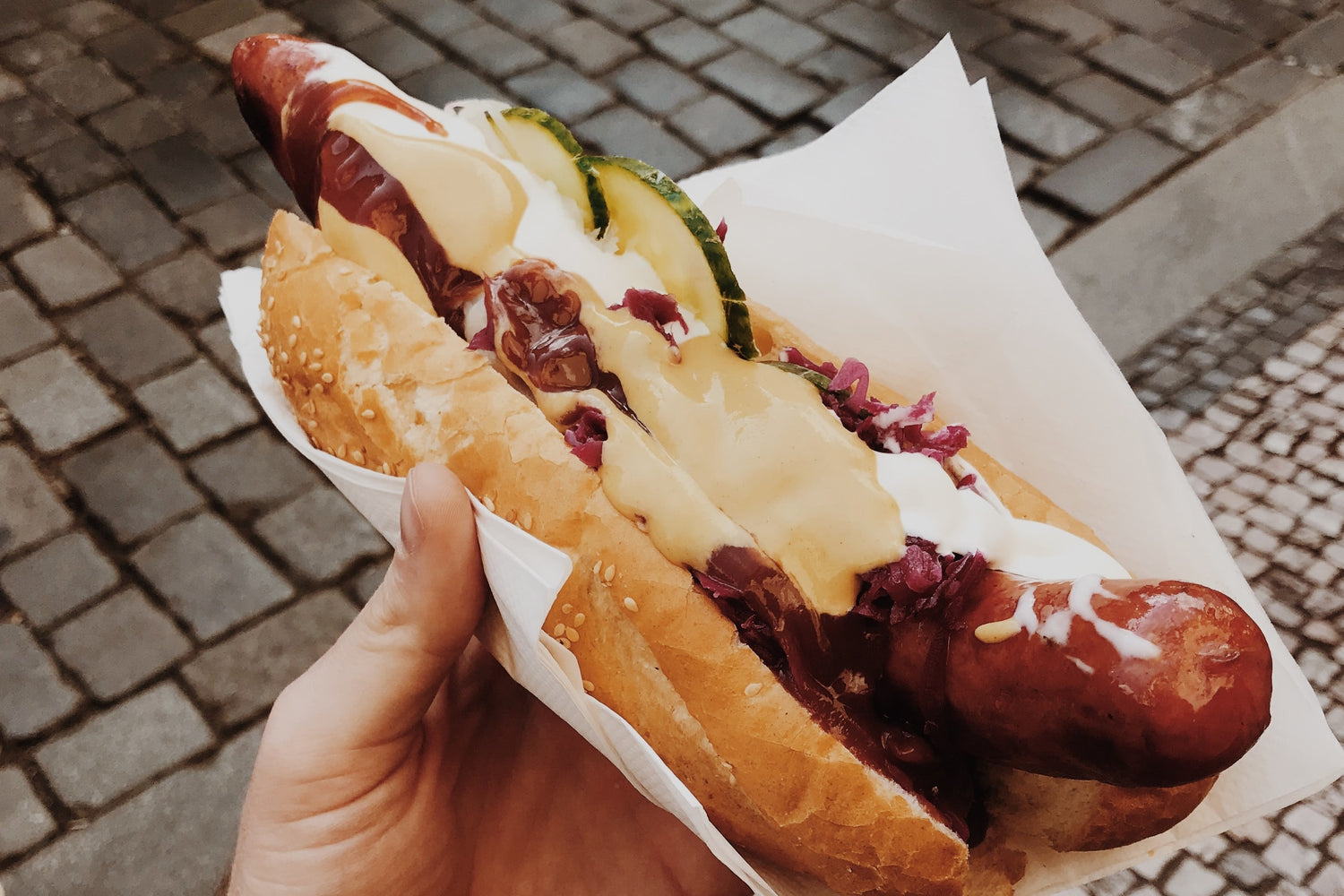 hand holding a cooked jumbo sausage in a hot dog roll with sauce