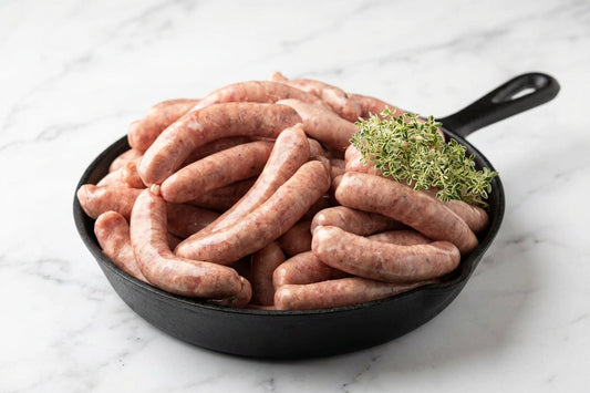 a black frying pan with raw pork chipolatas stacked on a black slate surface. 