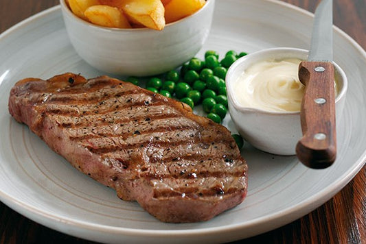 cooked sirloin steak pictured on a white plate with chips, peas and a garlic dip