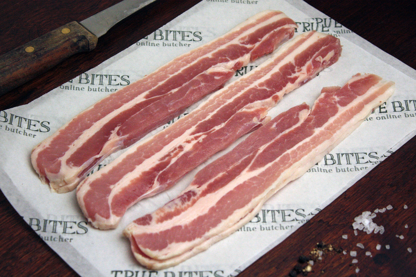 raw dry cured streaky bacon displayed on true bites branded greaseproof paper