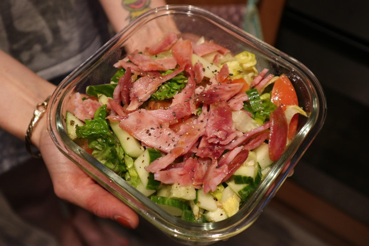 girls hands holding a bowl of salad topped with diced turkey bacon